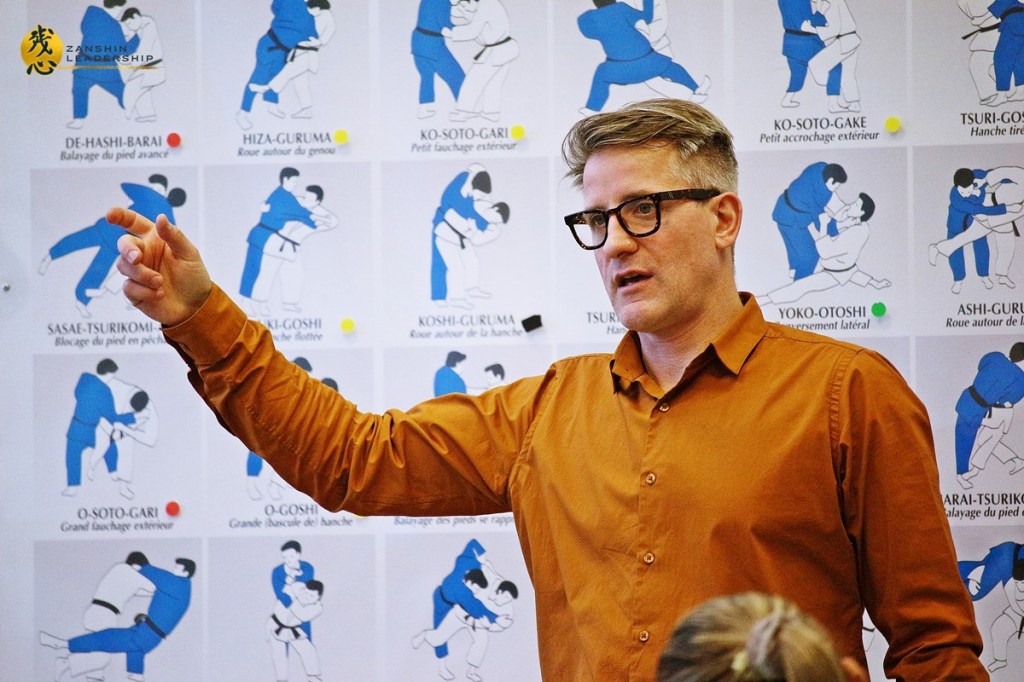 Matthaeus parlant à un groupe assis, avec des schémas au mur.